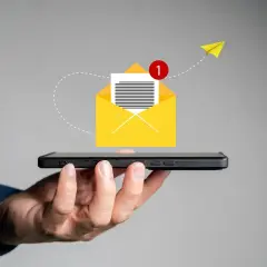 Dłoń trzyma smartfon, z którego wylatuje żółta koperta z powiadomieniem. Pomysł na to, co napisać w SMSie o urlop na żądanie.