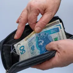 Ręce wkładają polskie banknoty 50 zł do portfela. Czy mam 58 lat i mogę przejść na emeryturę?