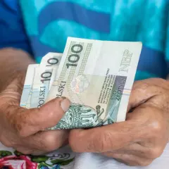 Dłonie starszej osoby trzymają banknoty 100 zł. Czy to wystarczy na godne życie przy minimalnej emeryturze w Polsce?