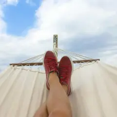 Nogi w czerwonych trampkach odpoczywają na hamaku pod błękitnym niebem. Czas na relaks i zastanowienie, ile urlopu za miesiąc pracy.