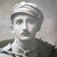 Młody żołnierz w czapce z orzełkiem, przypominający generała Nila, z wąsami i w wojskowym płaszczu.