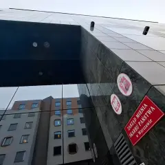 Nowoczesny budynek z lustrzaną fasadą odbija inne budynki. Na ścianie widnieje tablica "Zarząd Mienia Skarbu Państwa w Warszawie", co pokazuje jego komercyjny charakter.