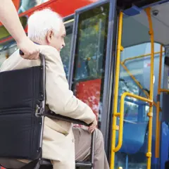 Starszy pan na wózku inwalidzkim, prawdopodobnie z chorobami kwalifikującymi do **2 grupa inwalidzka**, wsiada do autobusu z pomocą.