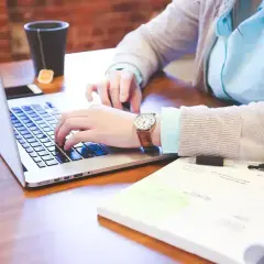 Osoba pracuje na laptopie, obok leży notatnik z długopisami. Różne rodzaje wykształcenia można zdobywać w ten sposób.