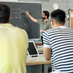Nauczyciel tłumaczy schemat na tablicy, studenci słuchają. To część jego pensum, by przekazać wiedzę.