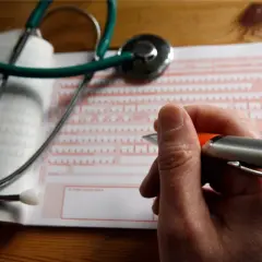 Lekarz wypełnia dokument, by ustalić, ile wynosi zasiłek chorobowy. Stetoskop leży obok.