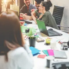 Uśmiechnięci millenialsi pracują razem przy biurku, otoczeni laptopami i tabletami.