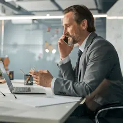 Mężczyzna w garniturze rozmawia przez telefon, patrząc na laptopa. To typowy dzień pracy CEO, co to znaczy? To znaczy, że zarządza firmą.