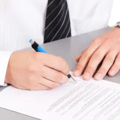 Mężczyzna w białej koszuli i krawacie podpisuje dokument. Na nadgarstku ma zegarek. To ważny moment, gdy dodaje klauzulę CV po angielsku.