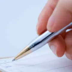 Dłoń pisze długopisem na kartce, przygotowując zwolnienie z lekcji.
