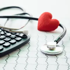 Kalkulator, stetoskop i czerwone serce na tle EKG symbolizują troskę o zdrowie i dobrowolne ubezpieczenie chorobowe.