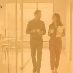 Para z kubkami kawy rozmawia w biurze, a w tle kobieta pracuje przy laptopie. To idealne miejsce dla hr.