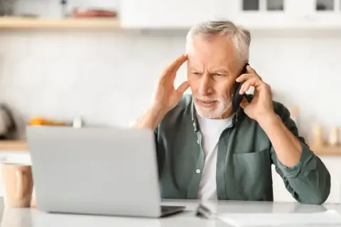 Zmartwiony mężczyzna rozmawia przez telefon, trzymając się za głowę. Może szuka siła wyższa powody problemów z laptopem.