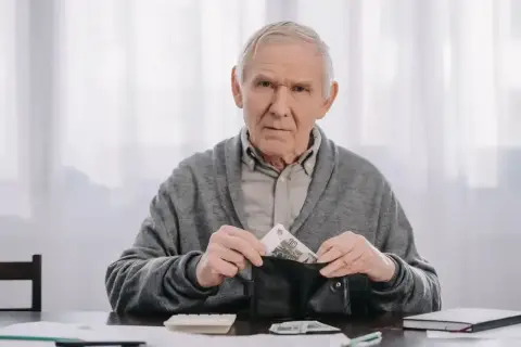 Zmartwiony senior wkłada pieniądze do portfela, planując kiedy na wcześniejszą emeryturę po nowemu.