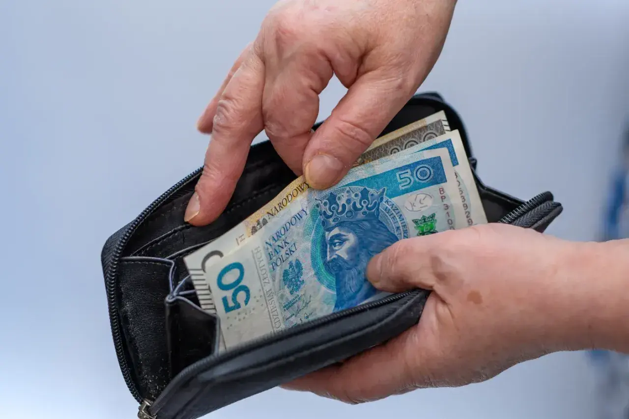 Ręce wkładają polskie banknoty 50 zł do portfela. Czy mam 58 lat i mogę przejść na emeryturę?