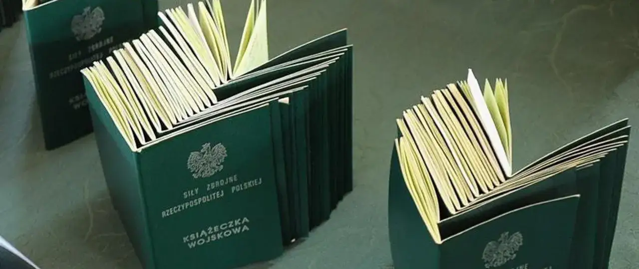 Książeczki wojskowe, symbol poboru do wojska, leżą otwarte, ukazując swoje strony.